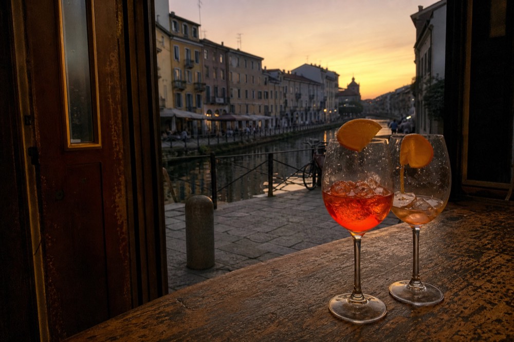 Two spritz glasses on a wooden bar counter with orange slices