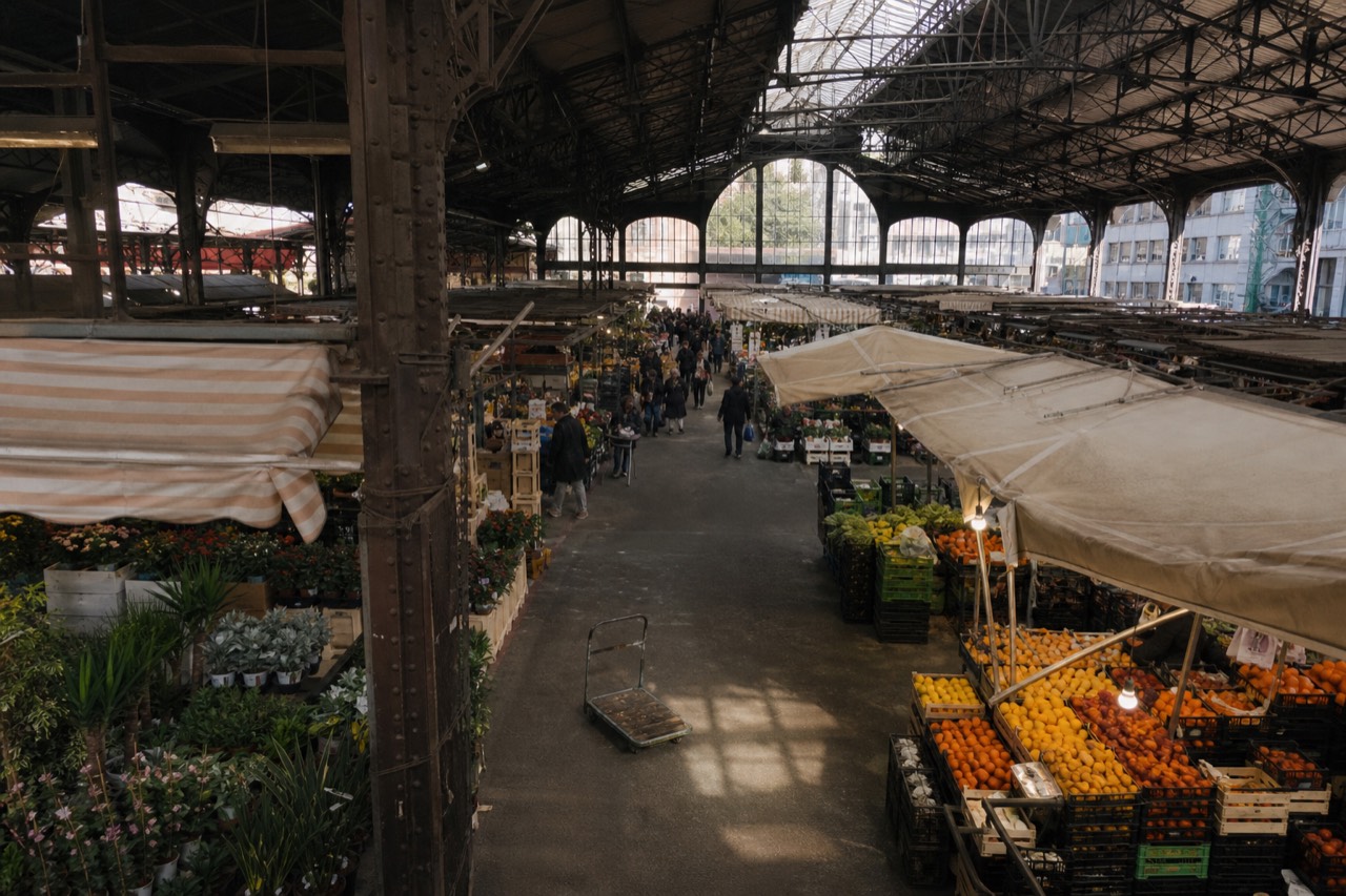 Milan covered market hall with produce stalls and shoppers under an iron and glass roof