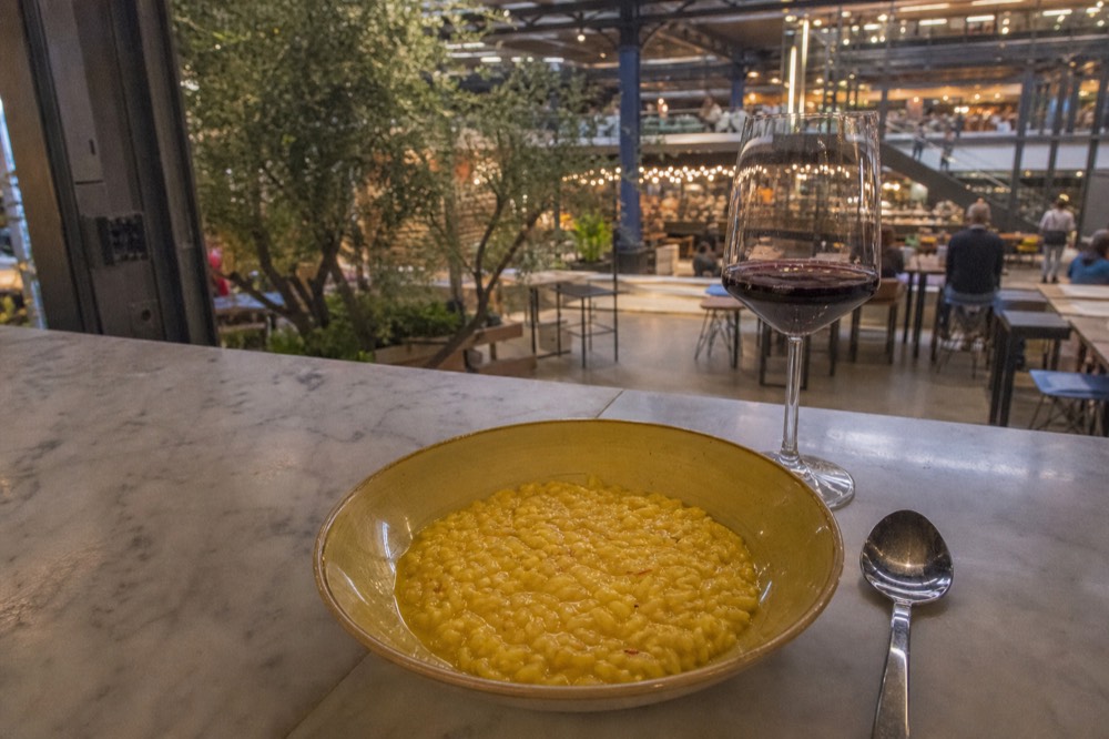 A saffron risotto served flat in a shallow bowl at a Milan food-hall counter
