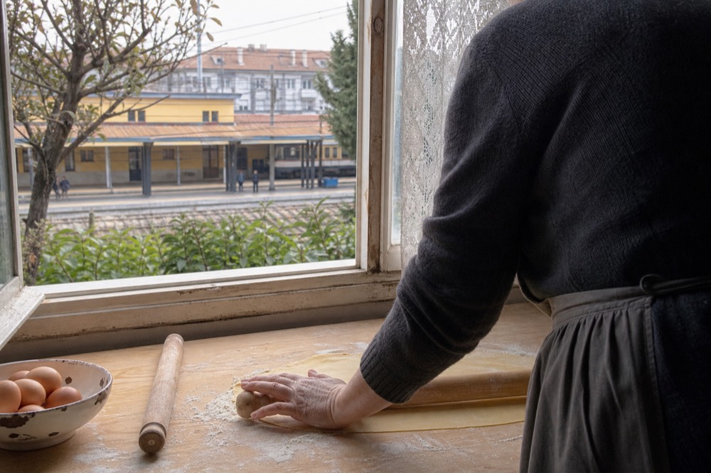 Hands rolling fresh pasta dough on a wooden board in a home kitchen