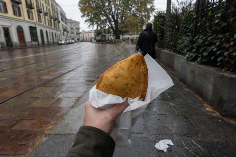 Person holding a fried panzerotto wrapped in paper on a Milan street