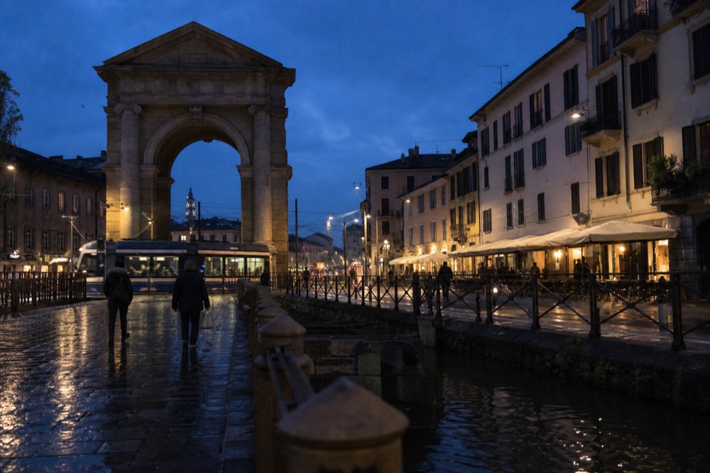 Milan street at dusk with lit shopfronts and people walking