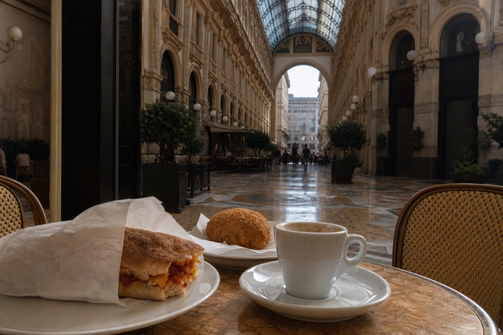 Paper-wrapped bread roll and fried snack on a cafe table in Milan