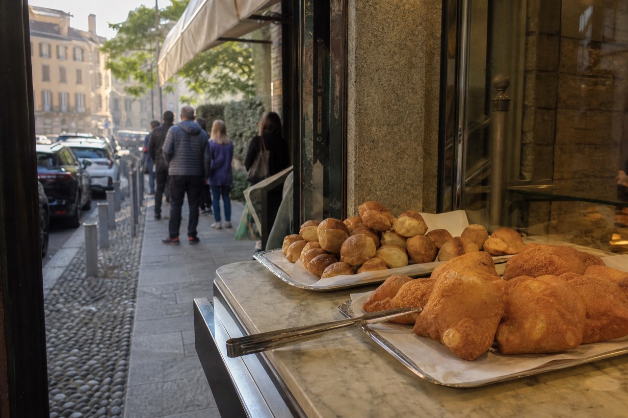 Bakery counter in Milan with fried pastries and bread rolls displayed under glass