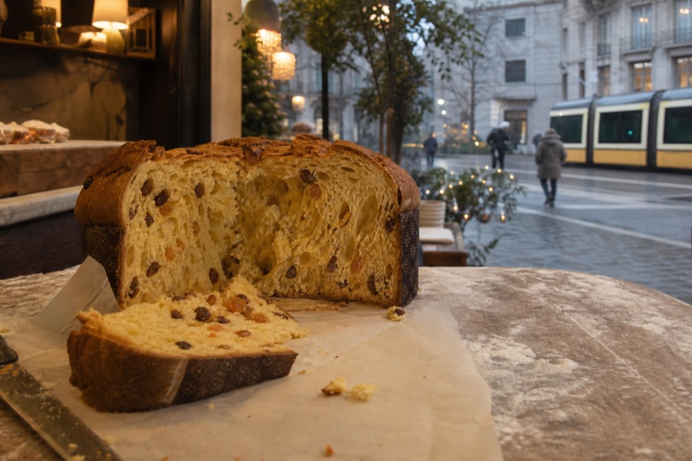 A cut slice of panettone showing an open elongated crumb with raisins and candied citrus peel