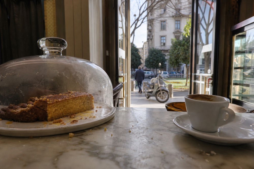A marble pastry counter with sliced cake under a glass dome in a Milan café
