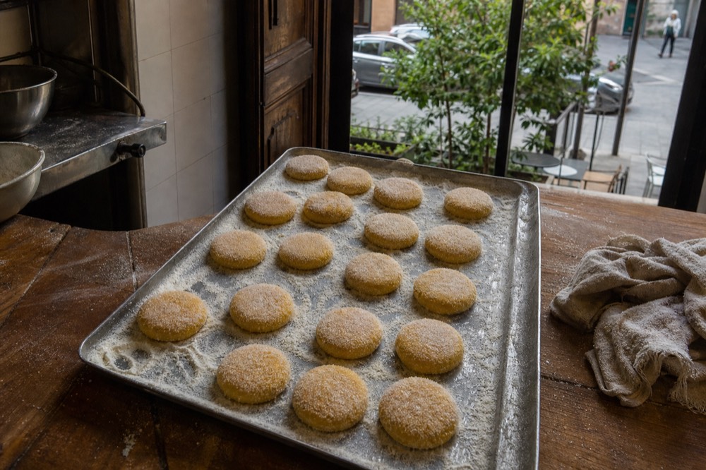 Small round cornmeal cakes dusted with sugar on a baking tray in a pastry kitchen