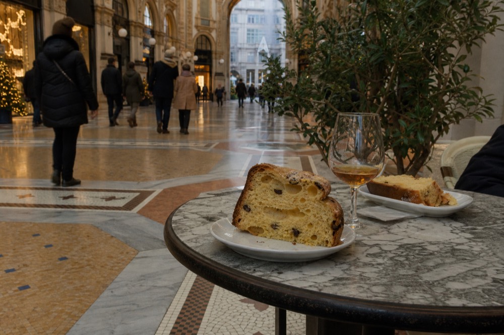 Slices of panettone beside a glass of sweet wine on a Milanese cafe table