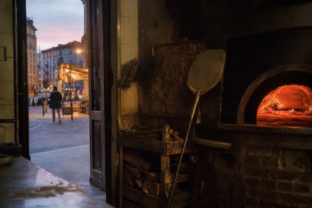 A wood-fired pizza oven glowing inside a Milan pizzeria kitchen