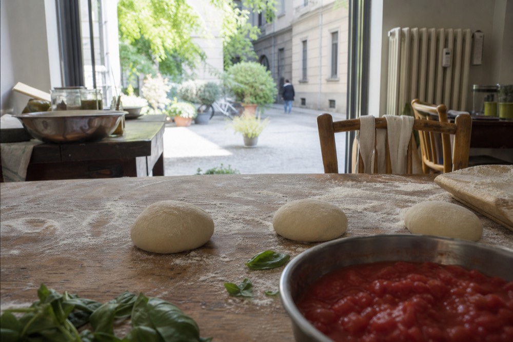 A floured wooden table with dough balls, tomatoes and basil ready for a cooking class
