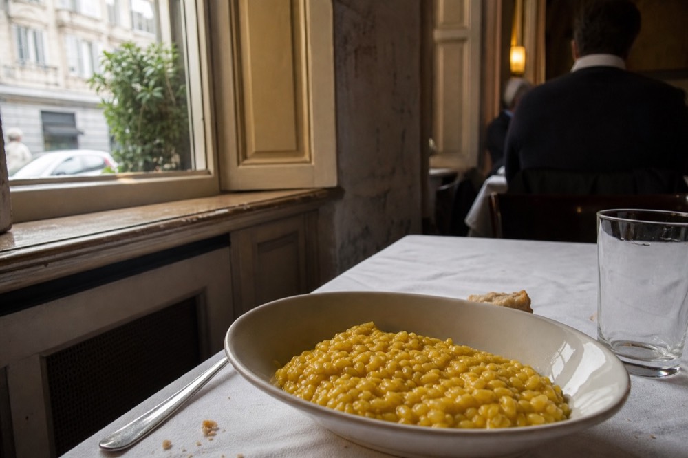 A golden saffron risotto in a shallow white bowl on a restaurant table