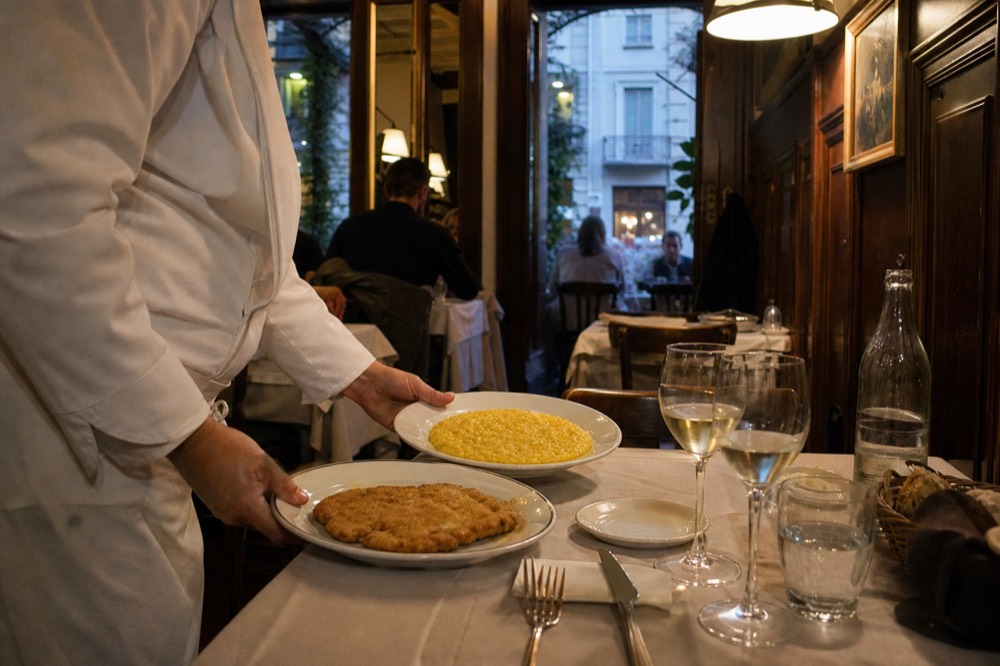 A traditional Milanese trattoria menu board listing risotto and cotoletta dishes