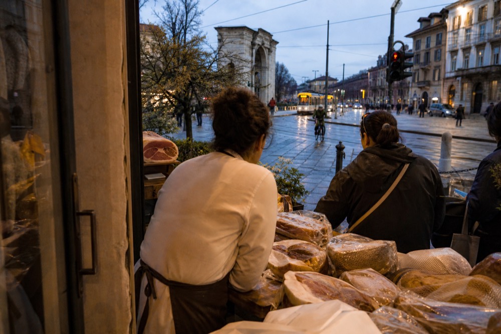 A customer speaking with a server at a Milanese deli counter