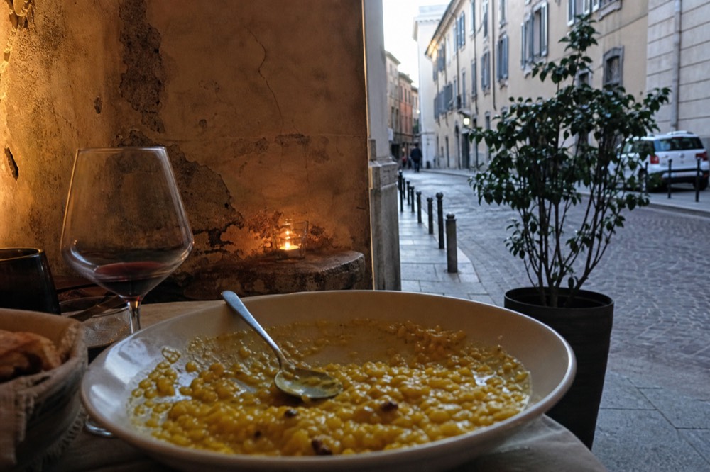 A saffron risotto in a shallow bowl with a spoon and a glass of red wine