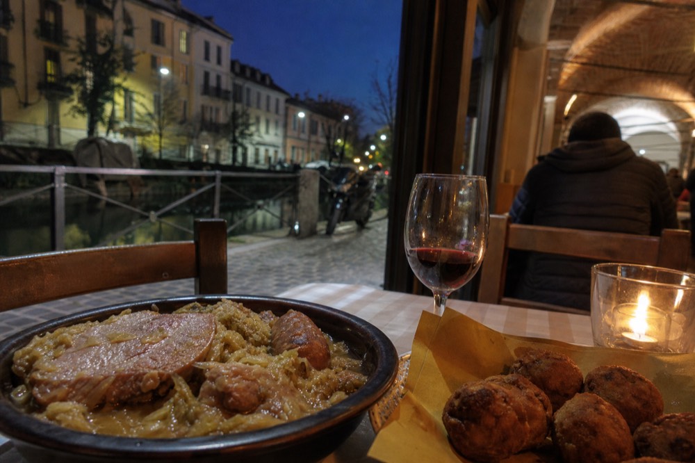 A bowl of cassoeula with dark cabbage and pork pieces next to fried mondeghili