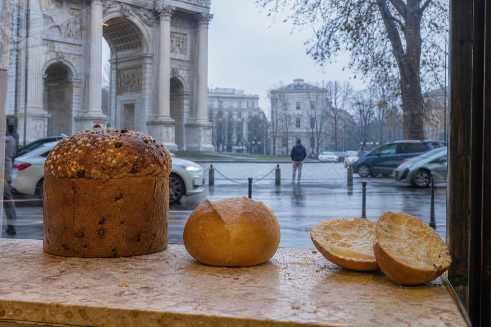 A dome-shaped panettone with candied fruit and a michetta roll beside it