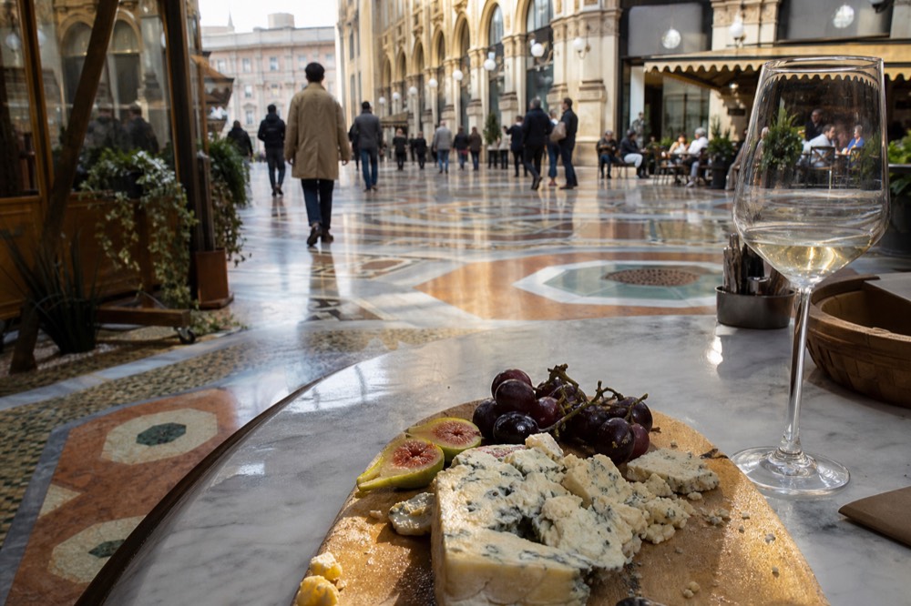 A cheese board with Gorgonzola, fresh fruit, and a glass of white wine on a counter
