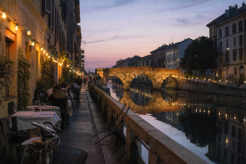 A canal-side street in Milan with outdoor restaurant tables at dusk