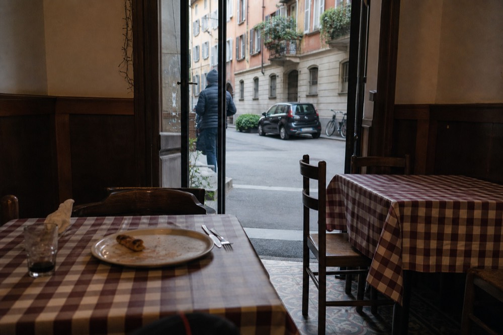 A traditional Milanese pizzeria interior with tiled floor and wooden chairs