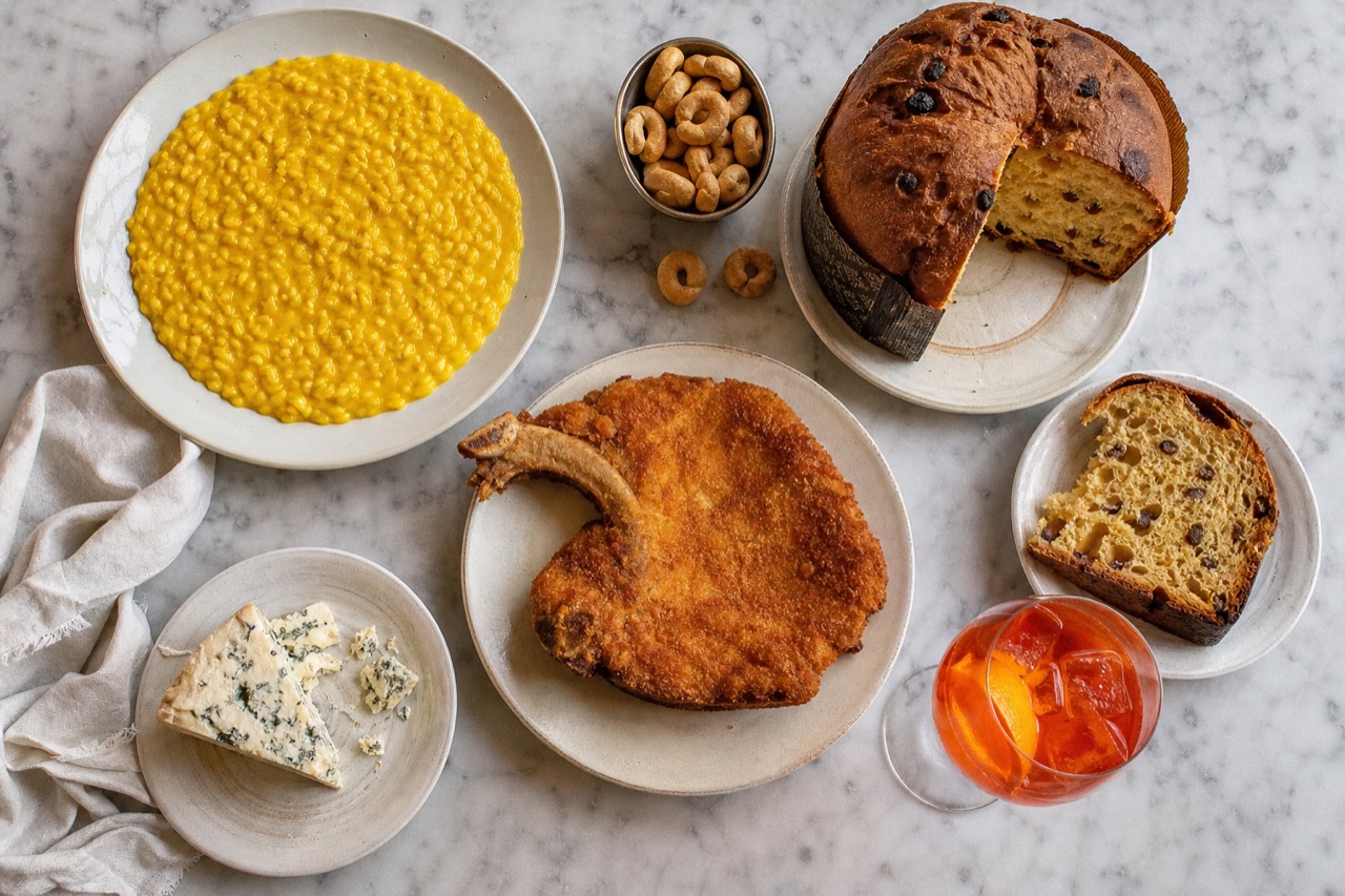 A Milanese tasting spread on a marble counter: saffron risotto, a breaded cotoletta, gorgonzola, panettone and a spritz